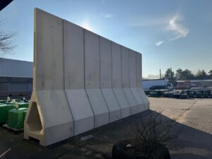 Foto wie einige mobilen Mauerelemente auf dem Hof vor blauem Himmel fotografiert sind. Die Mauer-Elemente aus Beton stehen auf einem stabilen Sockel in Dreiecksform